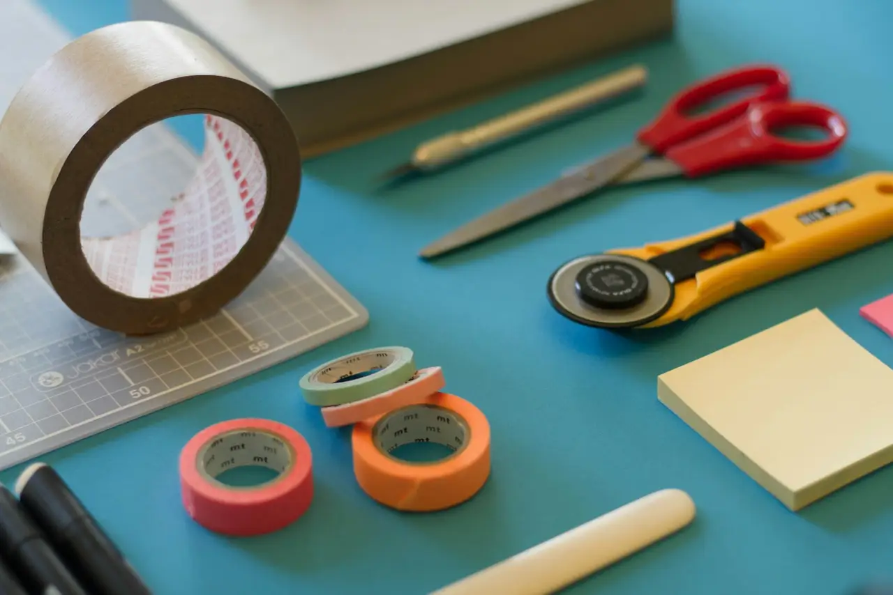 Craft supplies on a workbench: rolls of tape, scissors, a rotary cutter and a cutting mat.